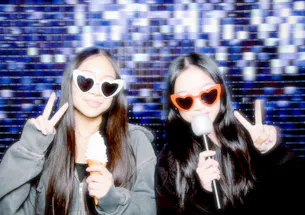 Two young women posing with microphones in front of the photo booth
