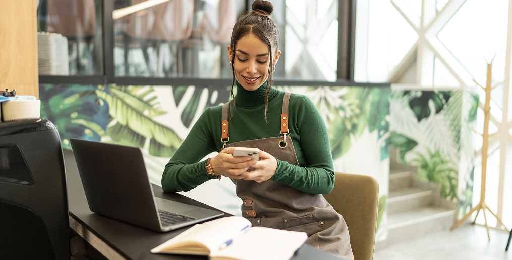 Business owner using a smartphone to access a digital business debit card while working on a laptop.