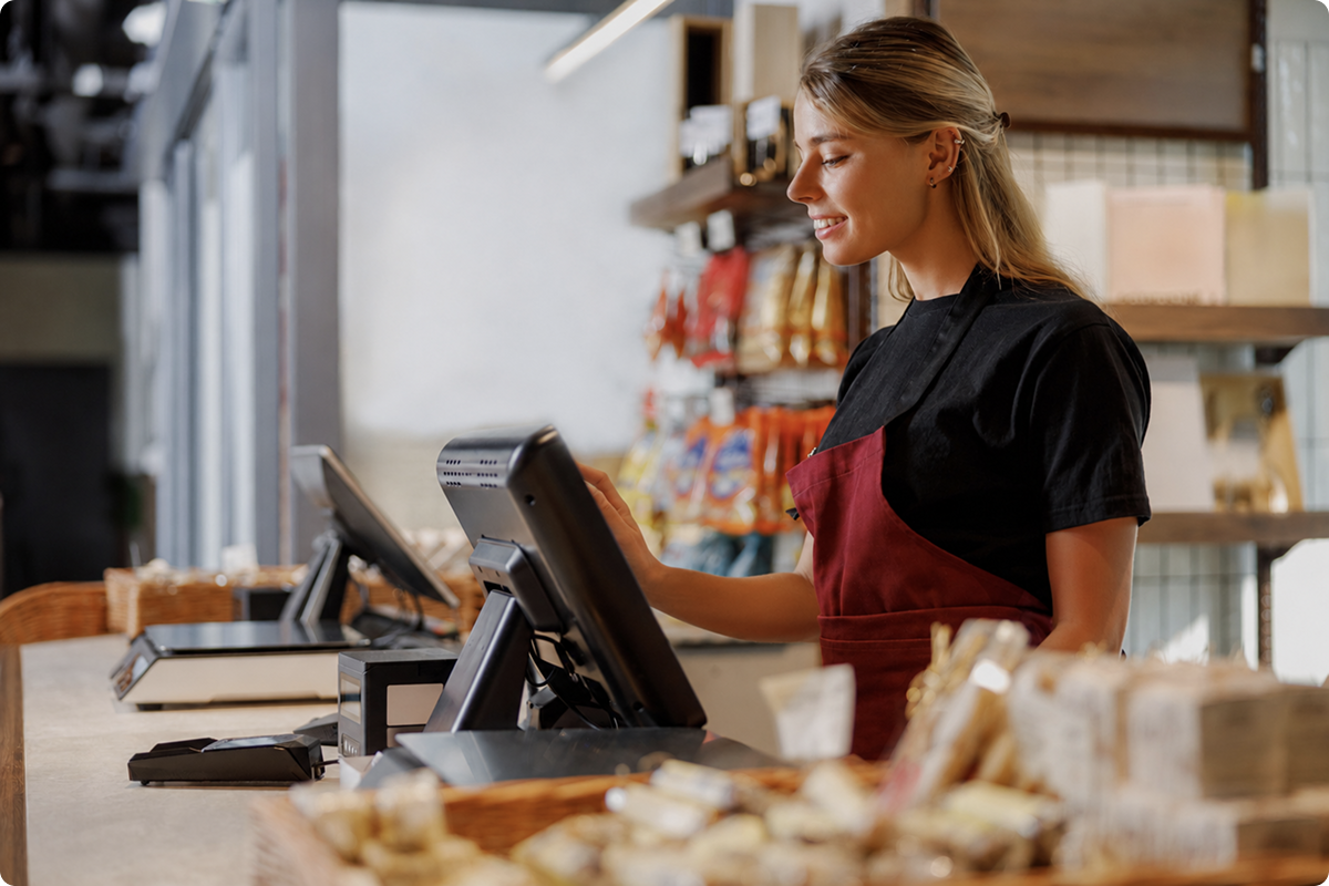 Fiscalisation and POS payment solutions for ISVs — smiling retail cashier operating a POS terminal at a food store counter, viva.com tax-compliant payments across Europe