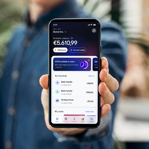 Merchant holding a smartphone displaying the viva.com business account interface, highlighting a zero payment fees UI, available balance, cashback program, recent transactions, and account management features.