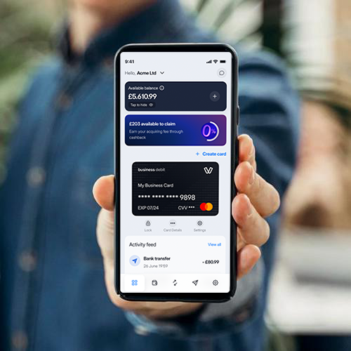 A merchant holding a smartphone showing the Viva.com app home screen with a zero payment fees cashback offer, a business debit card, and account balance details in pounds