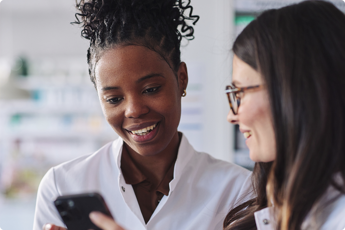Soluções de pagamento para farmácias — dois farmacêuticos a analisar opções de pagamento móvel num smartphone, Viva.com omnichannel payments para profissionais de saúde