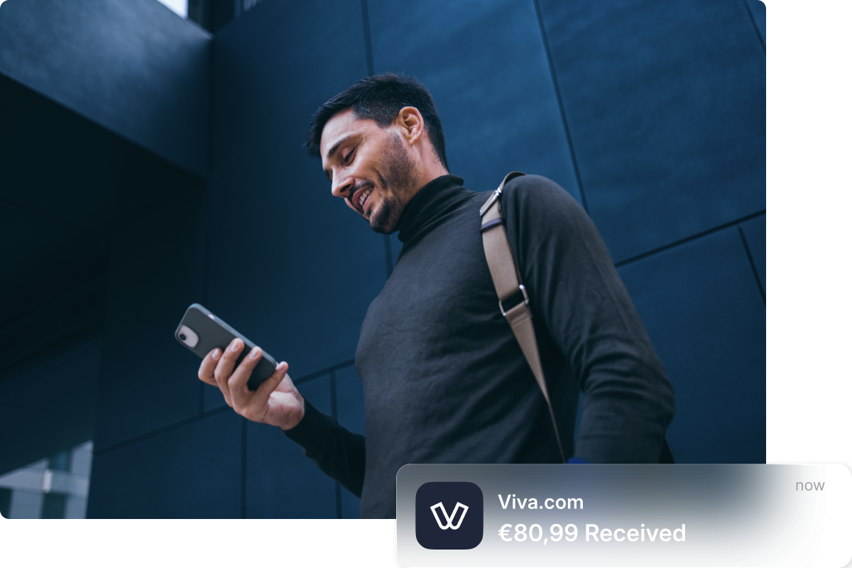 Mosolygó kereskedő, aki kültéren ellenőrzi telefonját, a Viva.com push értesítésével, amely „€80,99 Received" feliratot mutat, szemléltetve a kártyafizetések valós idejű elszámolását közvetlenül egy Viva.com-fiókba