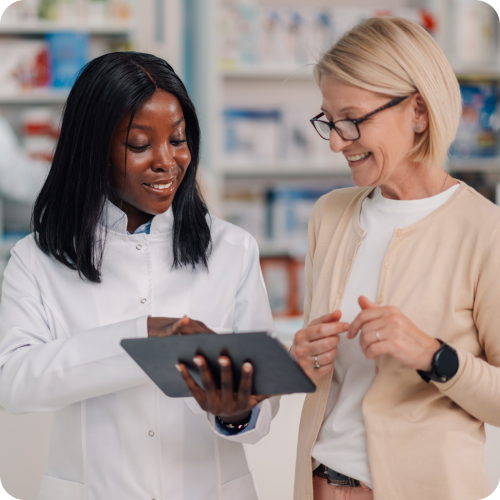 Pharmacist assisting a customer with healthcare payment or prescription information using a digital tablet in a pharmacy.