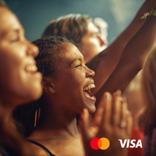 Visitantes de festival a efetuar pagamentos em bancas de eventos ao ar livre, representando os cashbacks, reembolsos e recompensas em tempo real da Viva.com, suportados pelo Mastercard Move e pelo Visa Direct