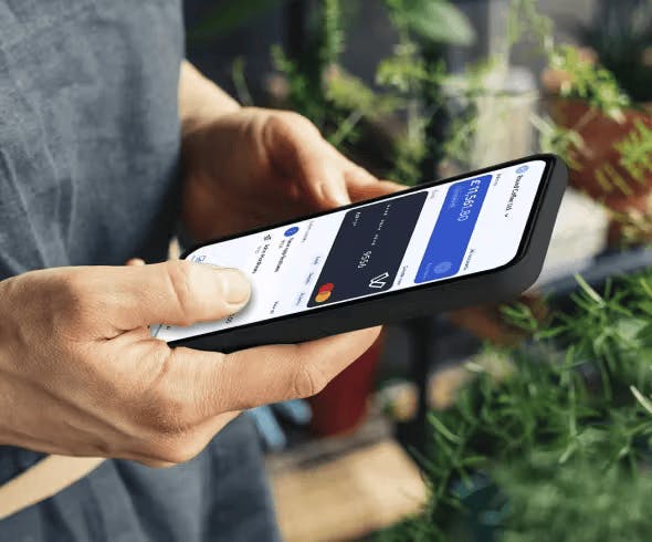 Person holding smartphone displaying Viva.com account interface showing card balance and transaction details in an outdoor setting