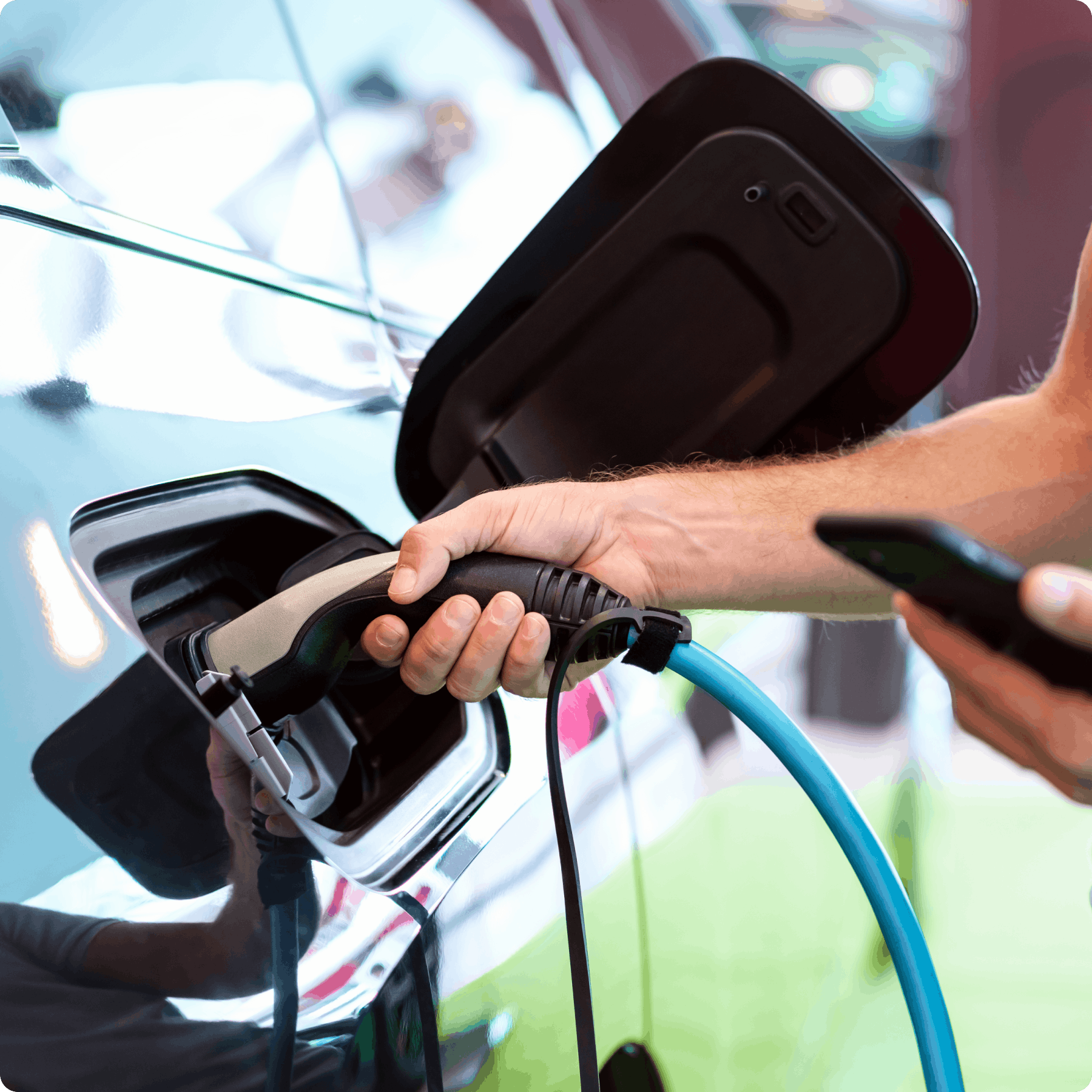Image showing an electric vehicle being plugged into a charging station. The person holds a smartphone, suggesting they used Viva.com’s unattended payment system to authorize and pay for the charging session.