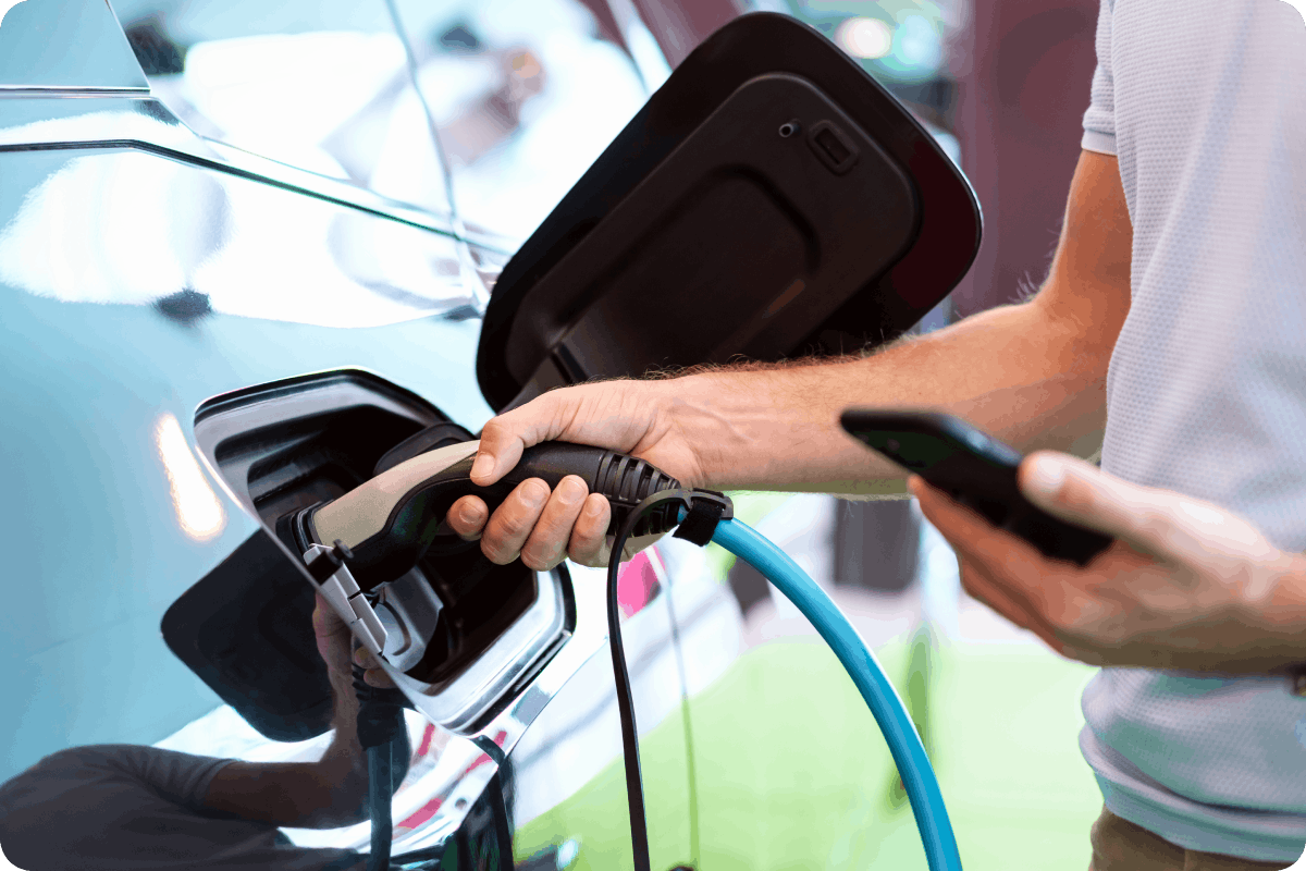 Image showing an electric vehicle being plugged into a charging station. The person holds a smartphone, suggesting they used Viva.com’s unattended payment system to authorize and pay for the charging session.