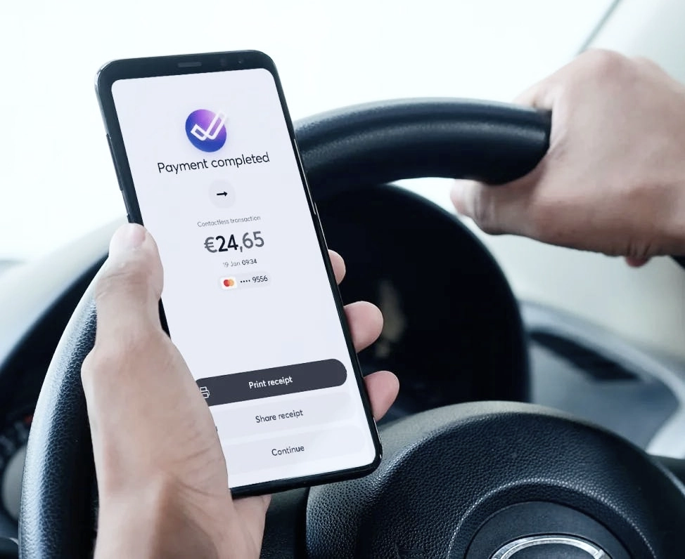 Driver holding smartphone displaying Viva.com payment completed screen showing 24.65 euro contactless transaction in vehicle, with options to print receipt, share receipt, and continue