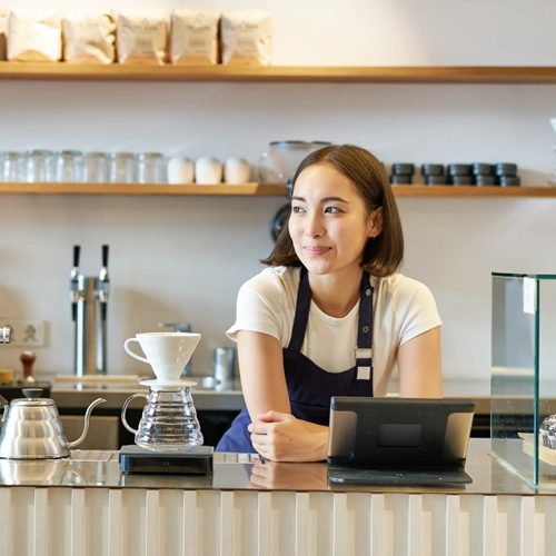 Cafe owner standing behind the counter with a tablet, representing the cost savings of using Viva.com Tap to Pay as a secure POS without extra hardware.
