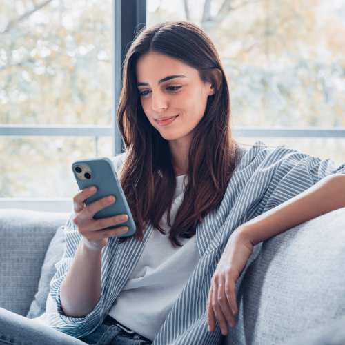Young woman sitting on a sofa using the Viva.com mobile app to manage her debit card.