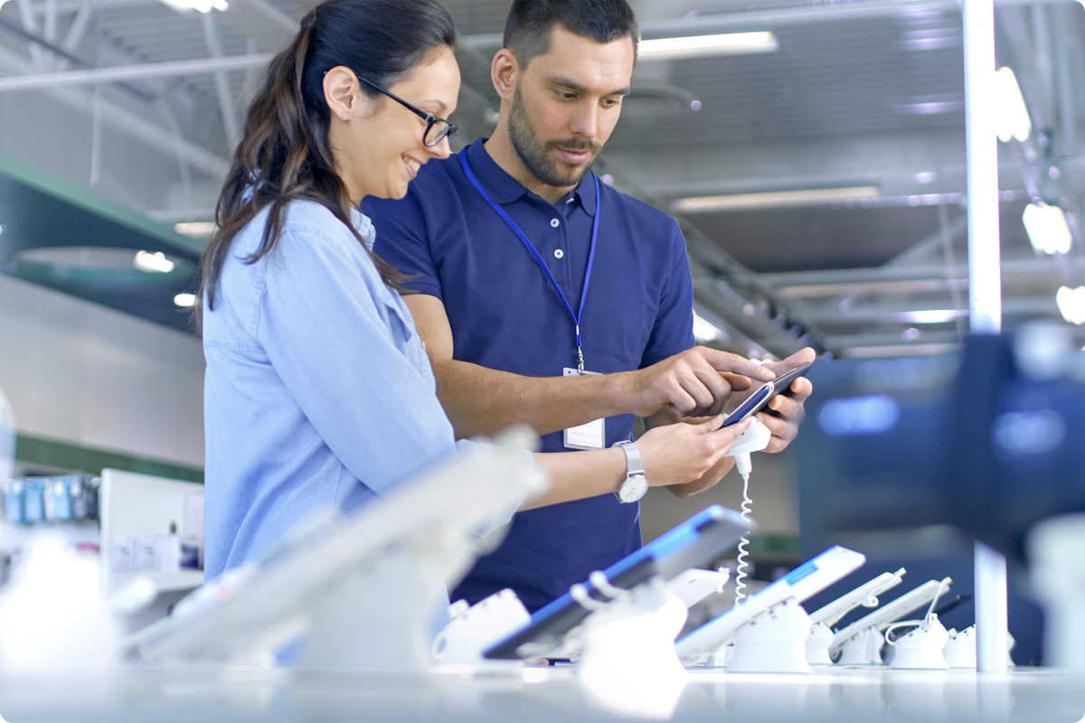 Solutions de paiement pour le commerce de détail — un conseiller de vente et un client qui explore des appareils au comptoir d'un magasin d'électronique, paiements POS omnicanal viva.com pour le secteur retail