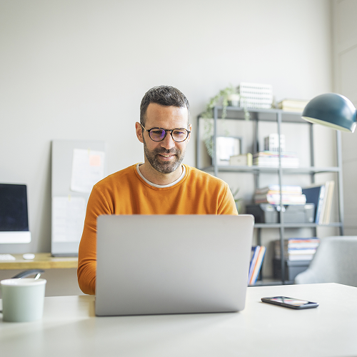 Smiling man with glasses working on a laptop in a modern office, representing a business owner managing secure and localised online payments through the viva.com payment gateway