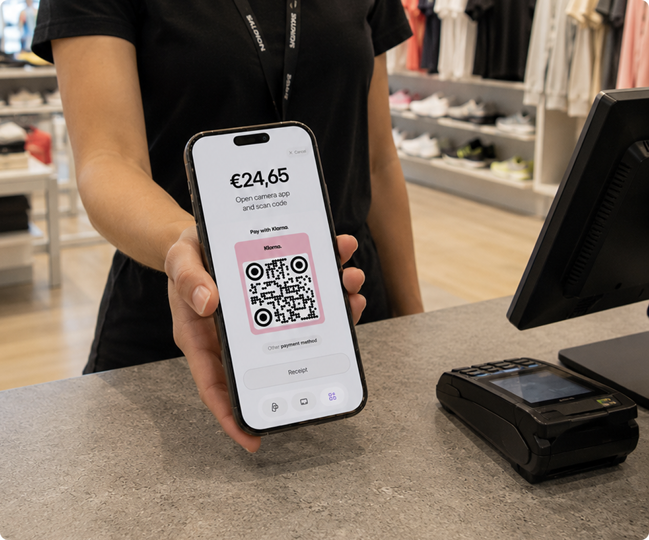 Pagamento Klarna in negozio con viva.com — addetto alle vendite che mostra il QR code Klarna su smartphone per pagamento flessibile in store, terminale viva.com al checkout