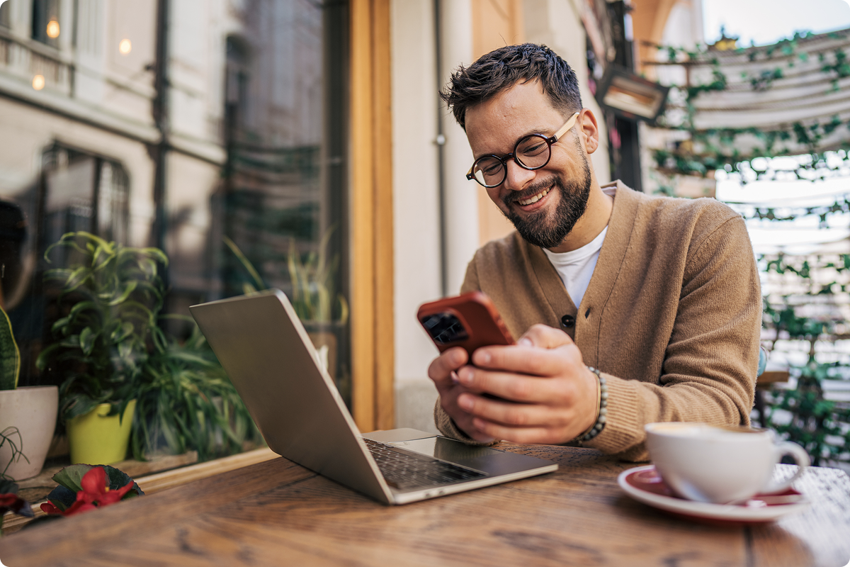 Business debit card instant activation — smiling professional managing expenses on smartphone and laptop at a café, viva.com business card with 0% transaction fees and cashback