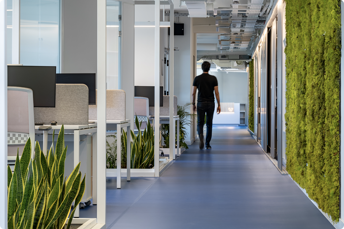 Technology at the core of payments — employee walking through viva.com's modern tech office with collaborative workspaces, greenery and illuminated viva.com logo, Europe's first tech bank