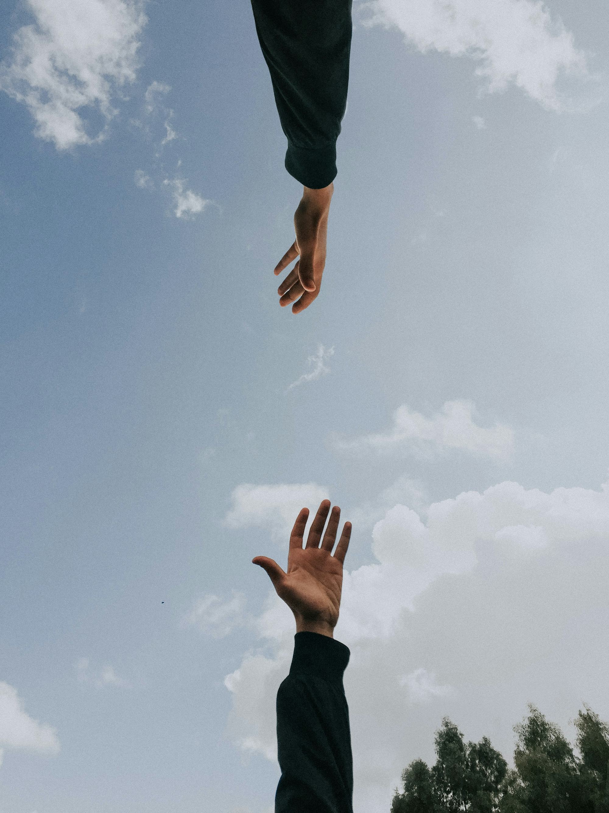 Kaksi kättä kurottaa toisiaan kohti sinisen taivaan alla.