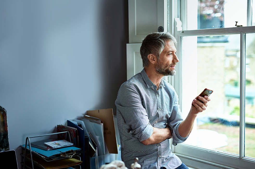 Man looking out the window with his phone in his hand