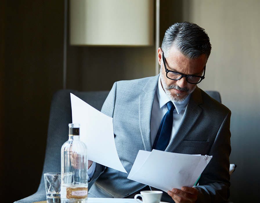 Man in grey suit and glasses sitting reading papers