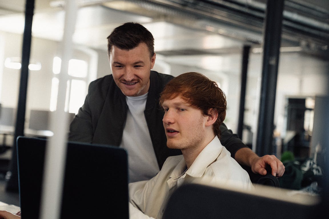 Tobias Saussele bespricht mit Mitarbeiter (Jona Großmann) im Büro die ToDos am Laptop