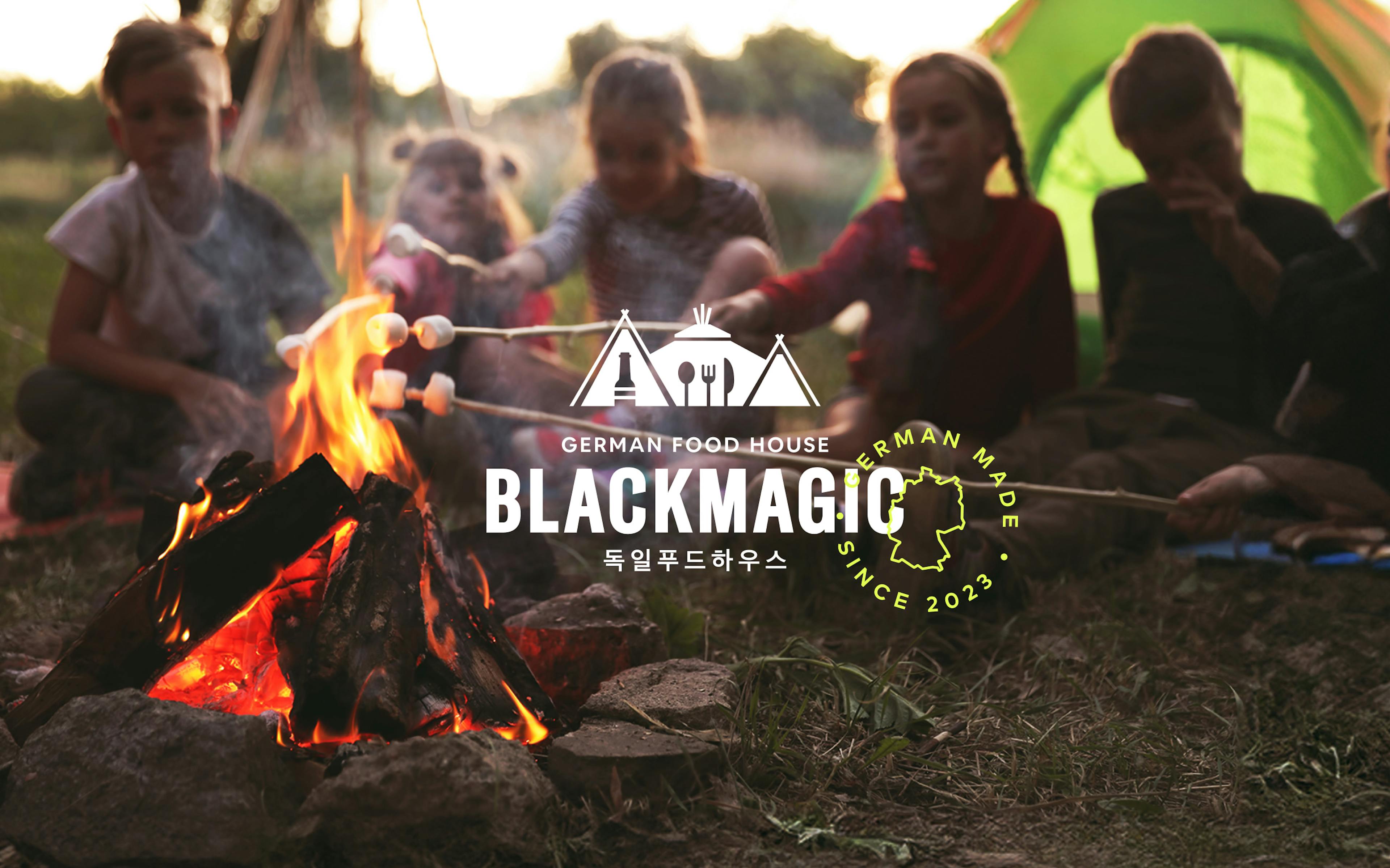 Weißes Blackmagic-Logo, im Hintergrund sieht man Kinder beim Stockbrot-Grillen in der Natur