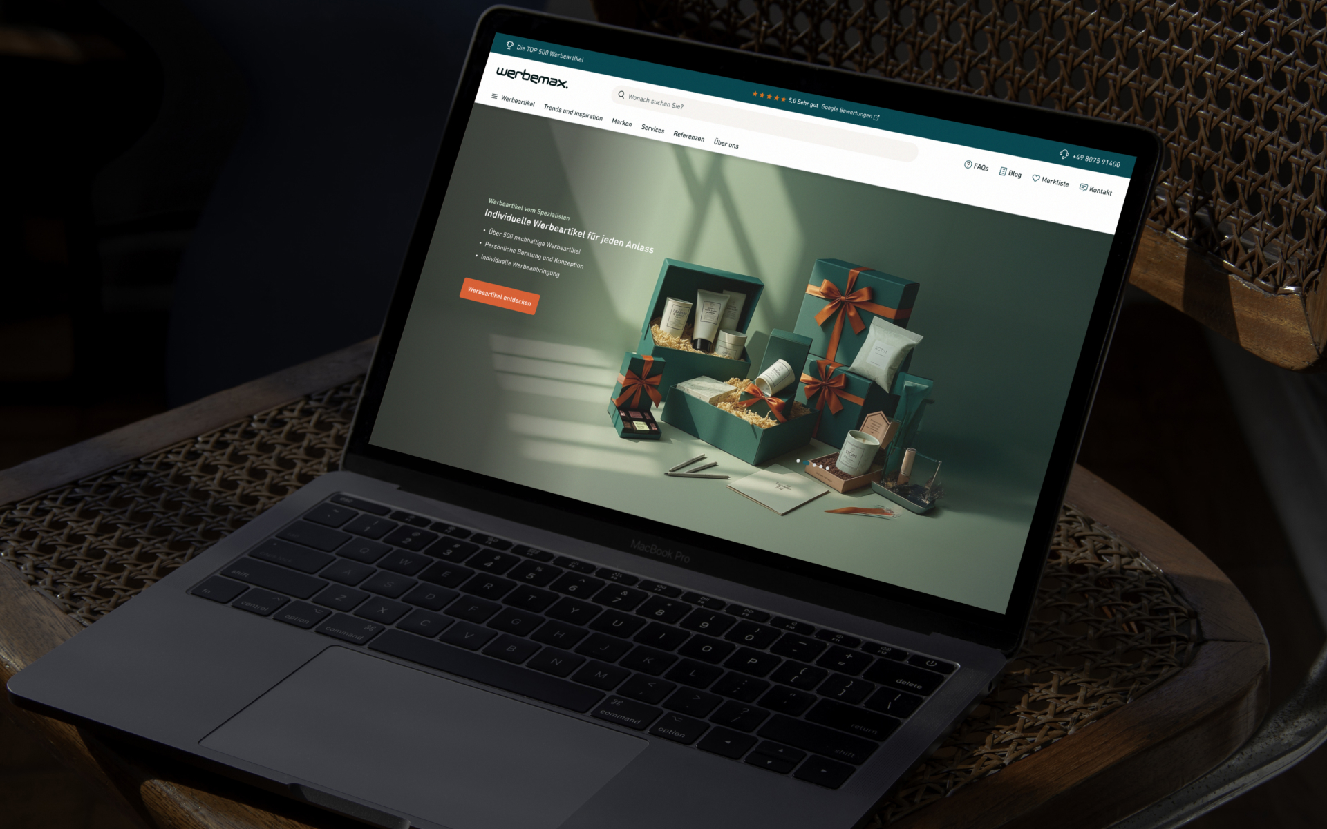 MacBook Pro auf Rattantisch zeigt Website mit grünen Geschenkboxen und Pflegeprodukten