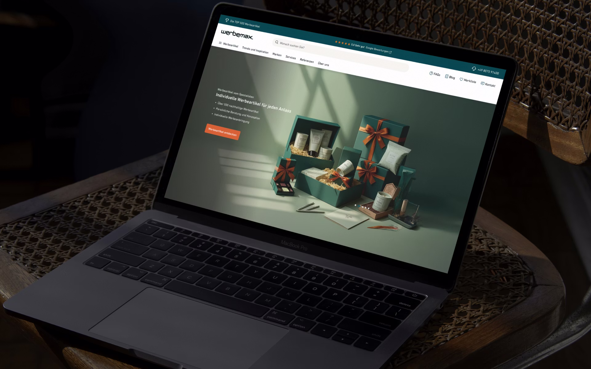 MacBook Pro auf Rattantisch zeigt Website mit grünen Geschenkboxen und Pflegeprodukten