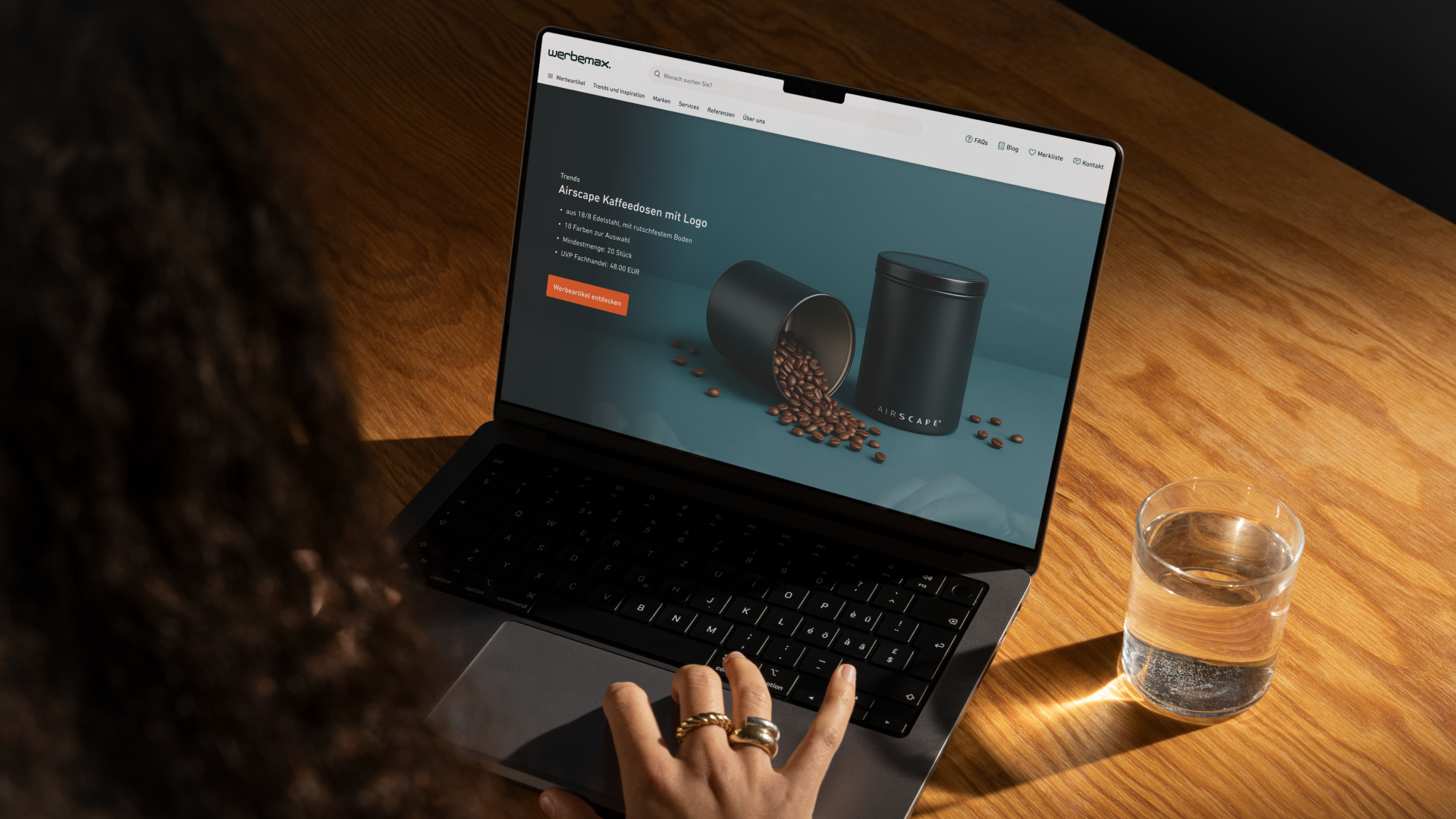 Person tippt auf Laptop, Bildschirm zeigt Weihnachts-Banner mit zwei schwarzen Thermobechern