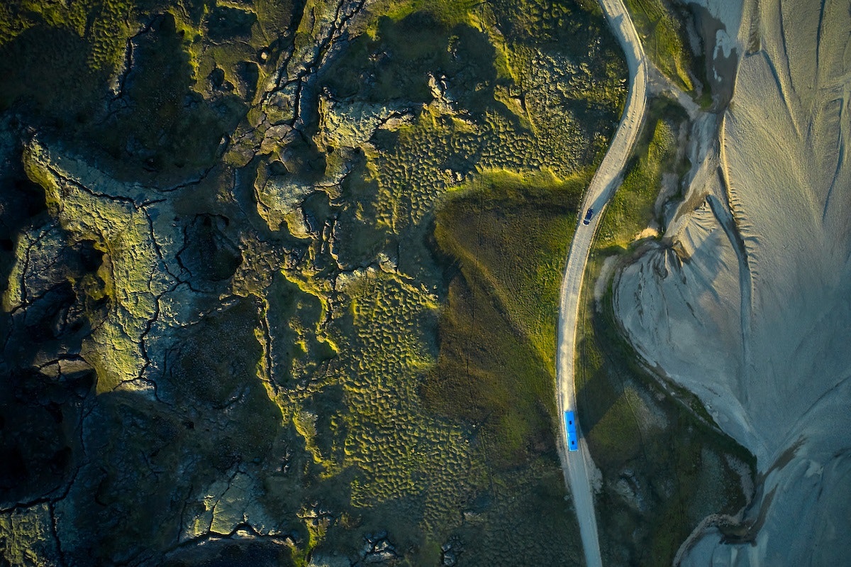A drone shot of cars driving via a lonely road in the Icelandic wilderness