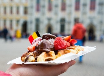 Traditional Belgian dessert - waffle with strawberry and cream on the background of Brugge, Belgium