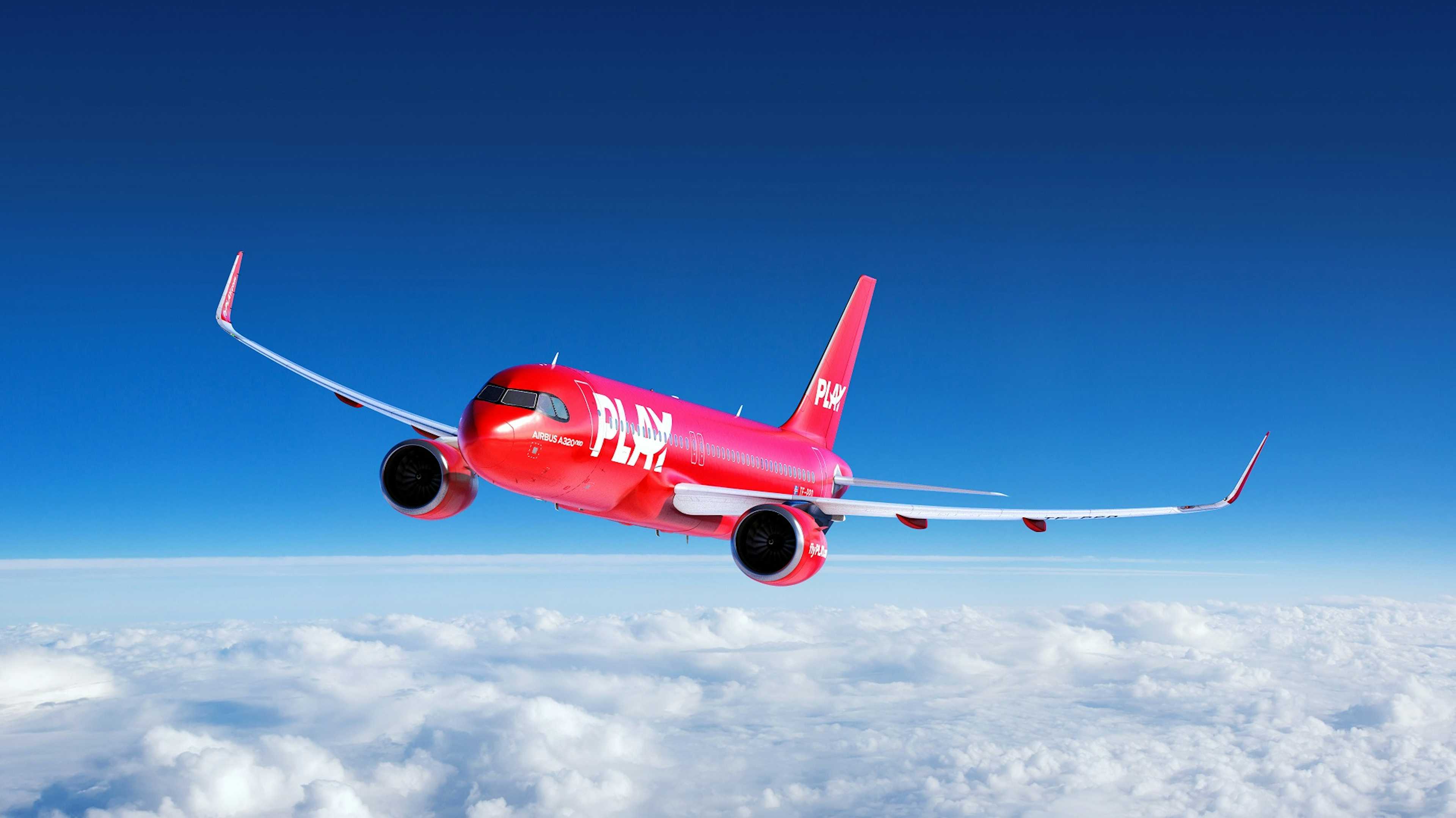 A red PLAY aircraft flying the blue skies above the clouds