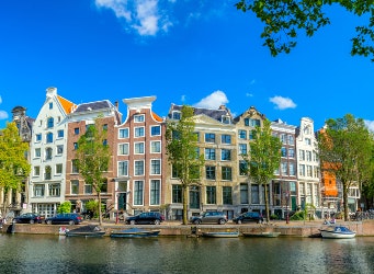 Panoramic view of Amsterdam street over the water. Famous narrow houses against the blue sky