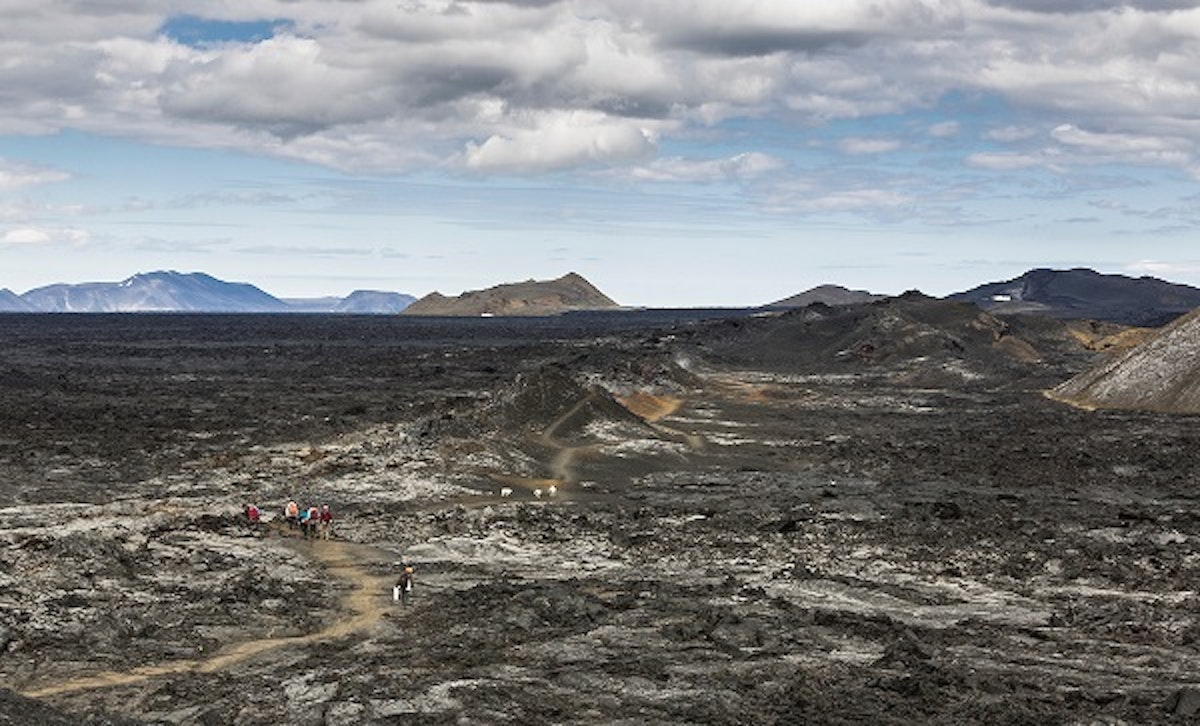 A panoramic view over an unbuilt lava field in Iceland with hikers on a trail