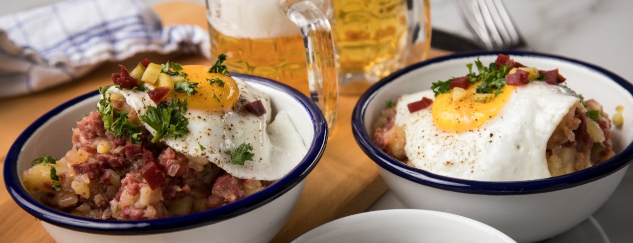Hamburg Labskaus is a delicacy with corned beef, potatoes, beetroot, pickled gherkins, fried egg, herring and beer on marble table