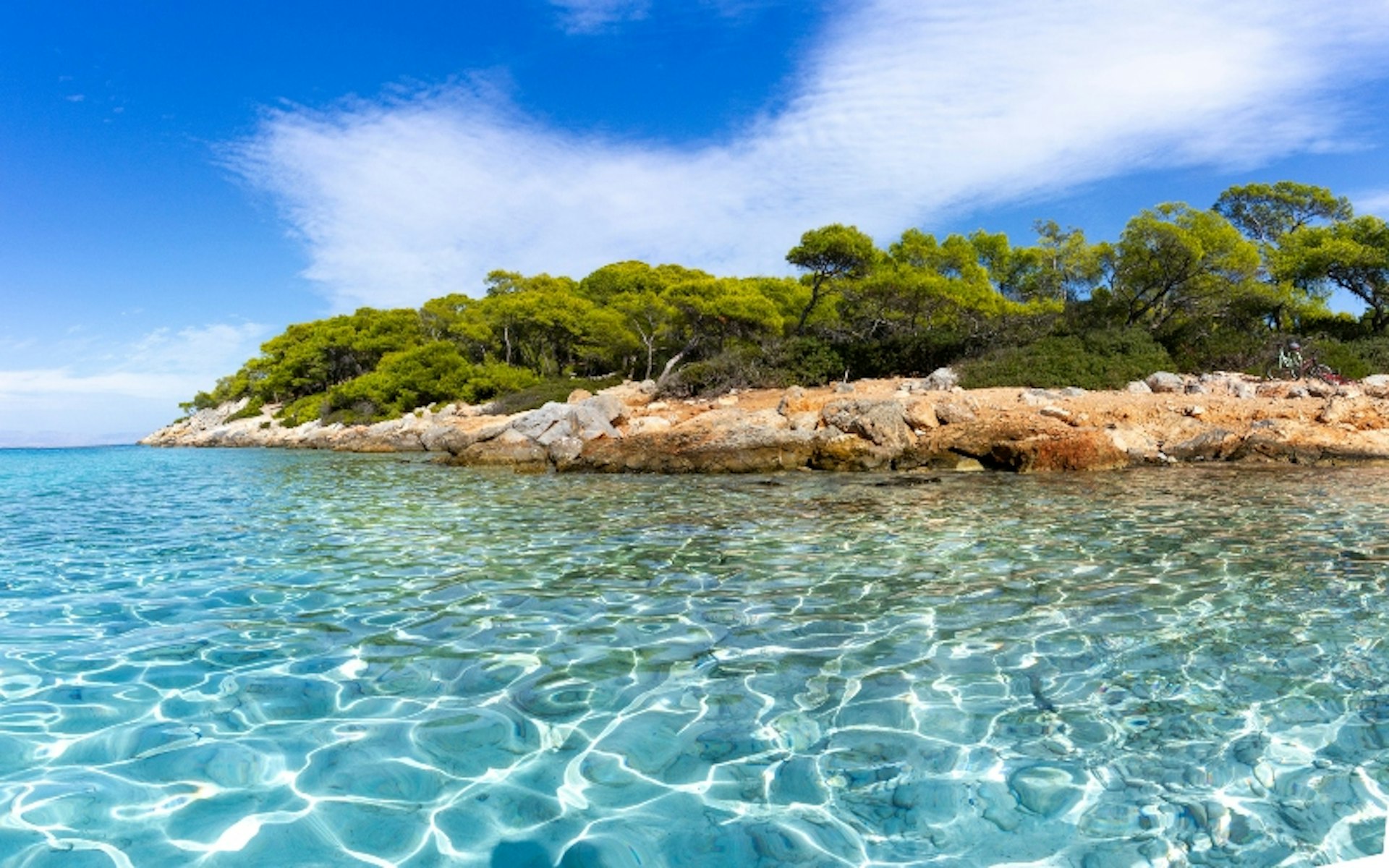 view of the Aponissos beach, Greece, where turquoise waters meet with the green forest and the clear blue sky.