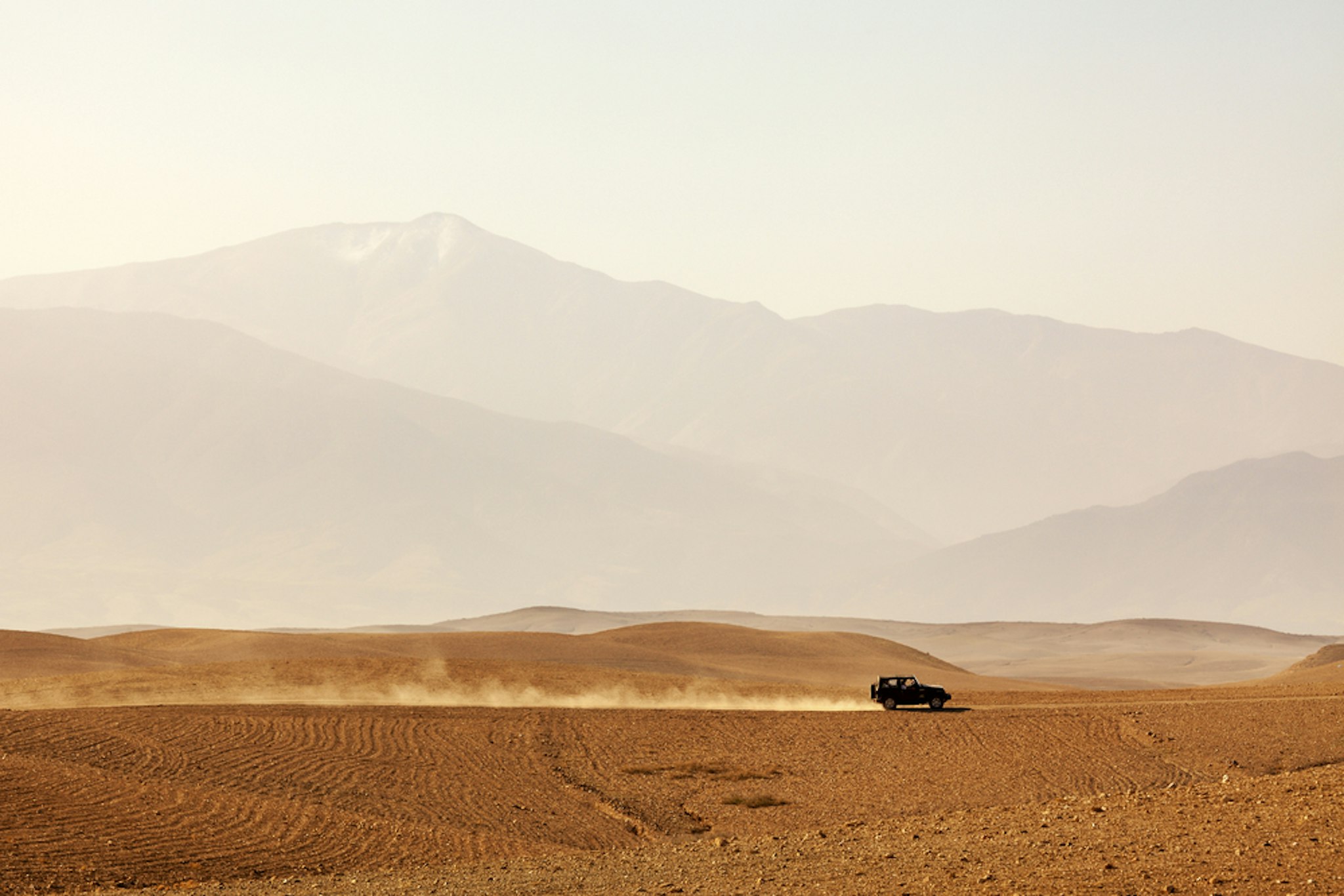 Off-road vehicle driving through Agafay desert, Morocco, Atlas Mountains vanishing in haze