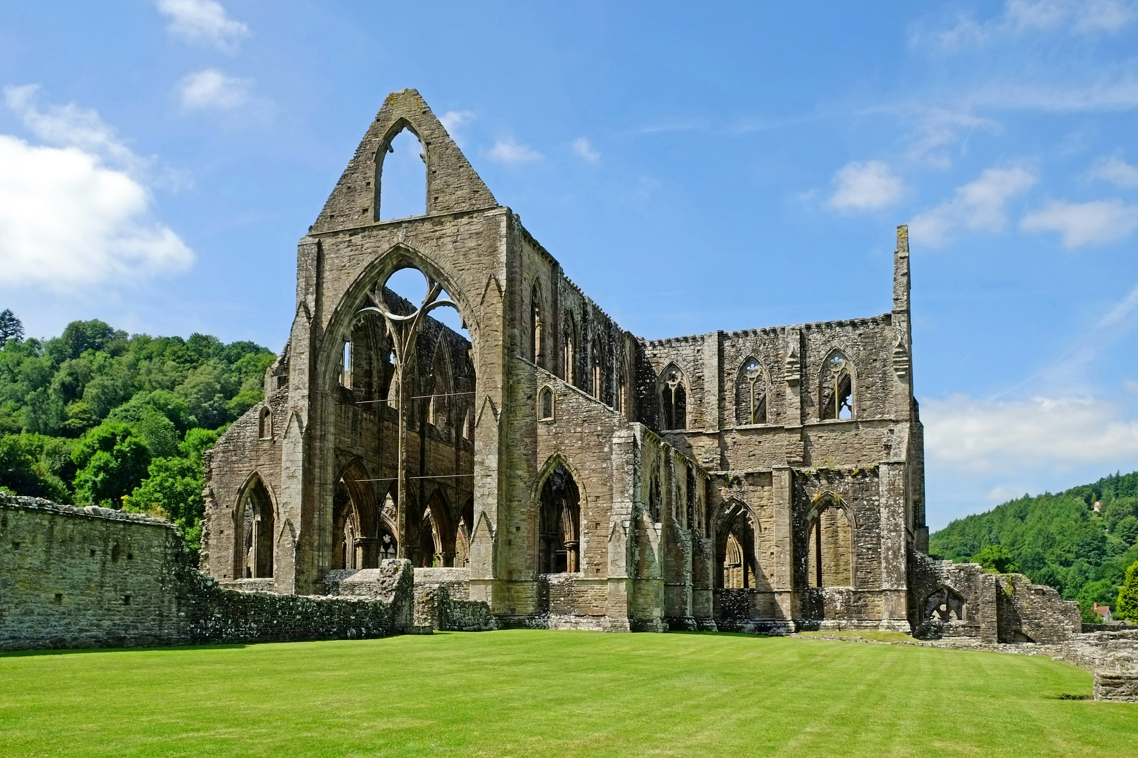 Tintern Abbey klaustrið í Wales með skógi vaxnar hlíðar allt í kring og bláan himinn í bakgrunni