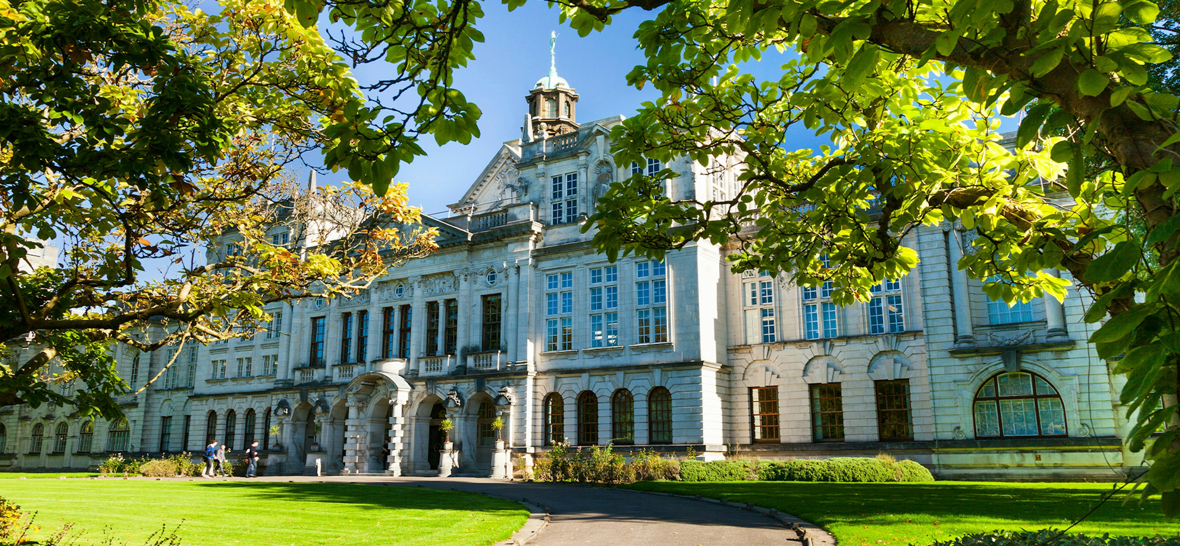 A beautiful white building in Cardiff with green grass and trees in front. 