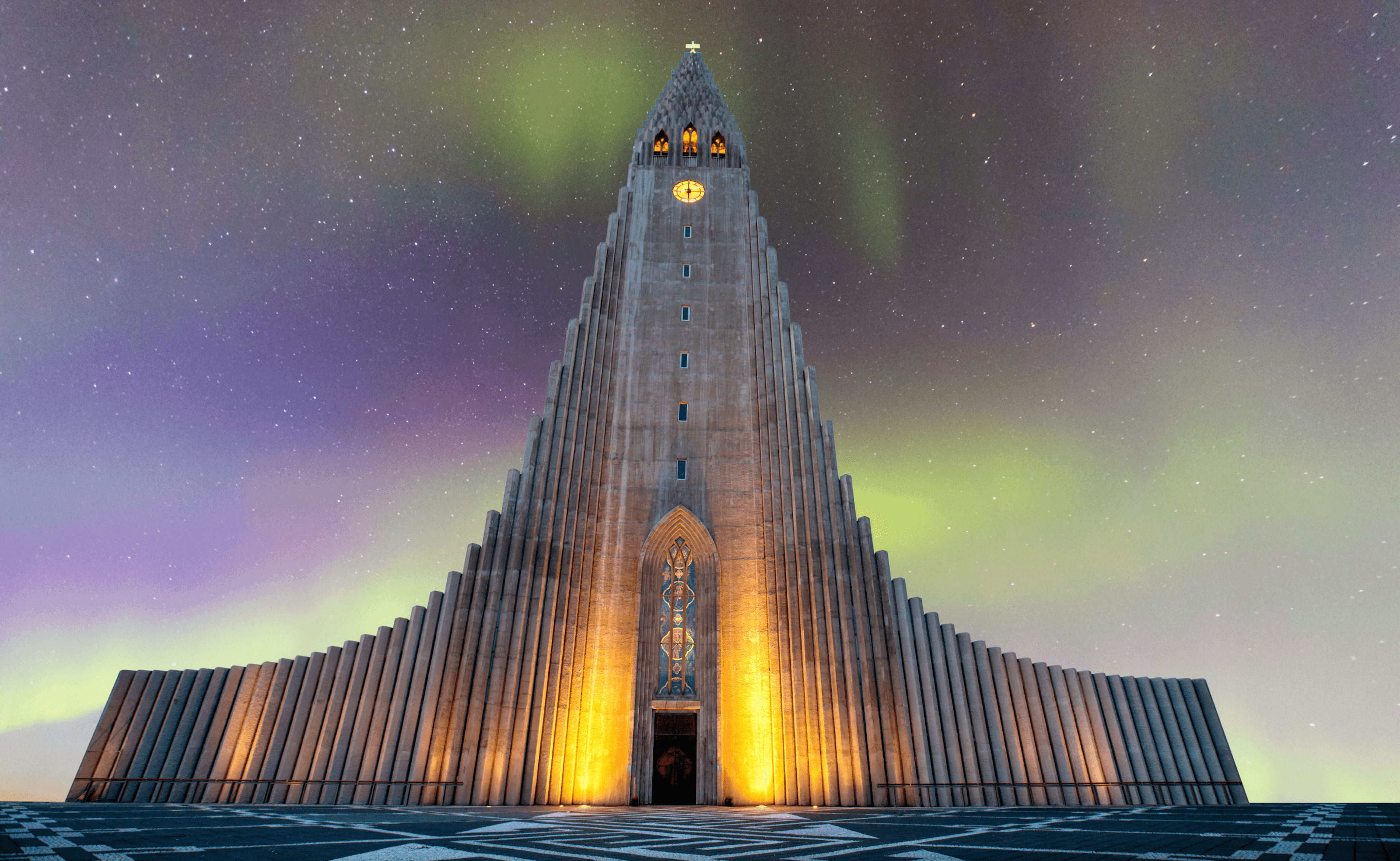 Hallgrímskirkja church at night with a lit up facade and northern lights in the sky above