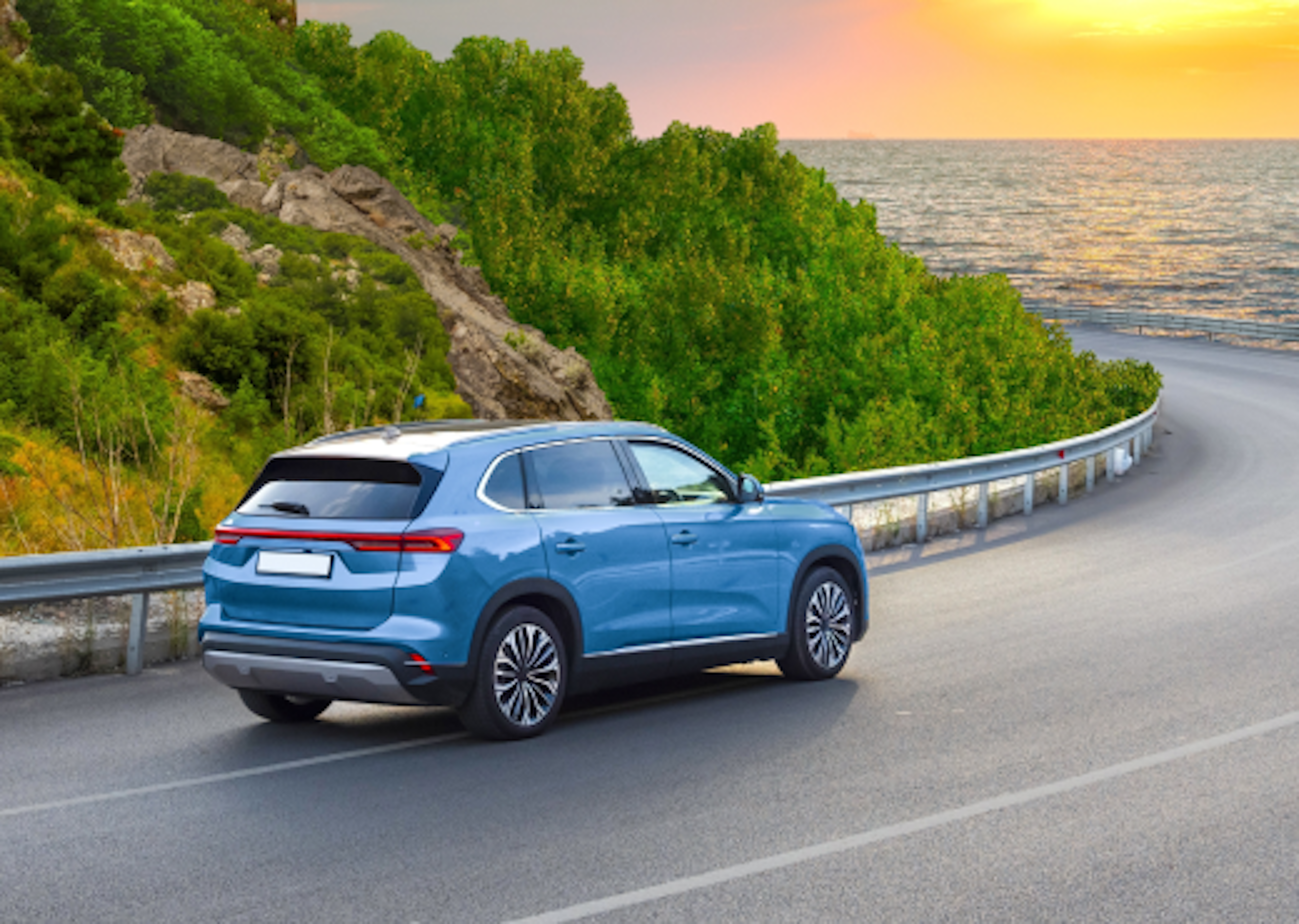 Blue car driving down a road with sunset and the sea ahead.