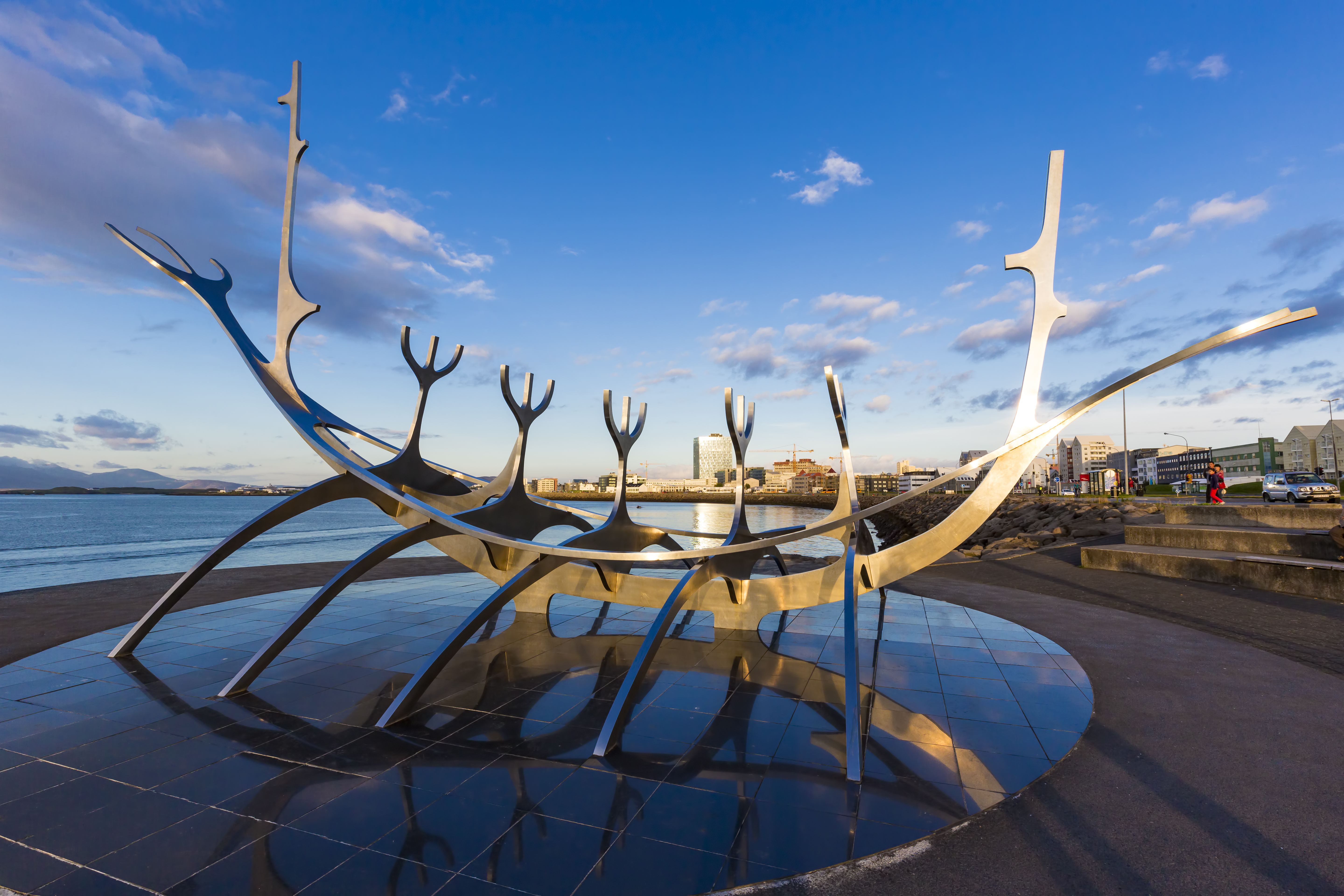The Sun Voyager (Solfar) sculpture in Reykjavik set against the scenic coastline with Mount Esja in the background under a blue sky.
