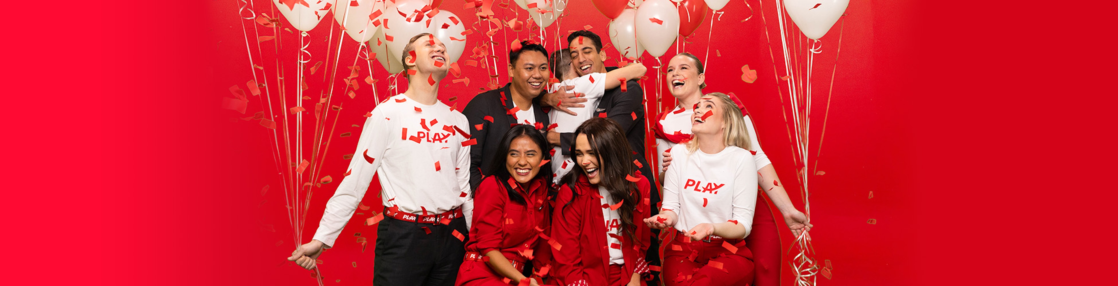 PLAY crew members celebrating with balloons in front of a red background