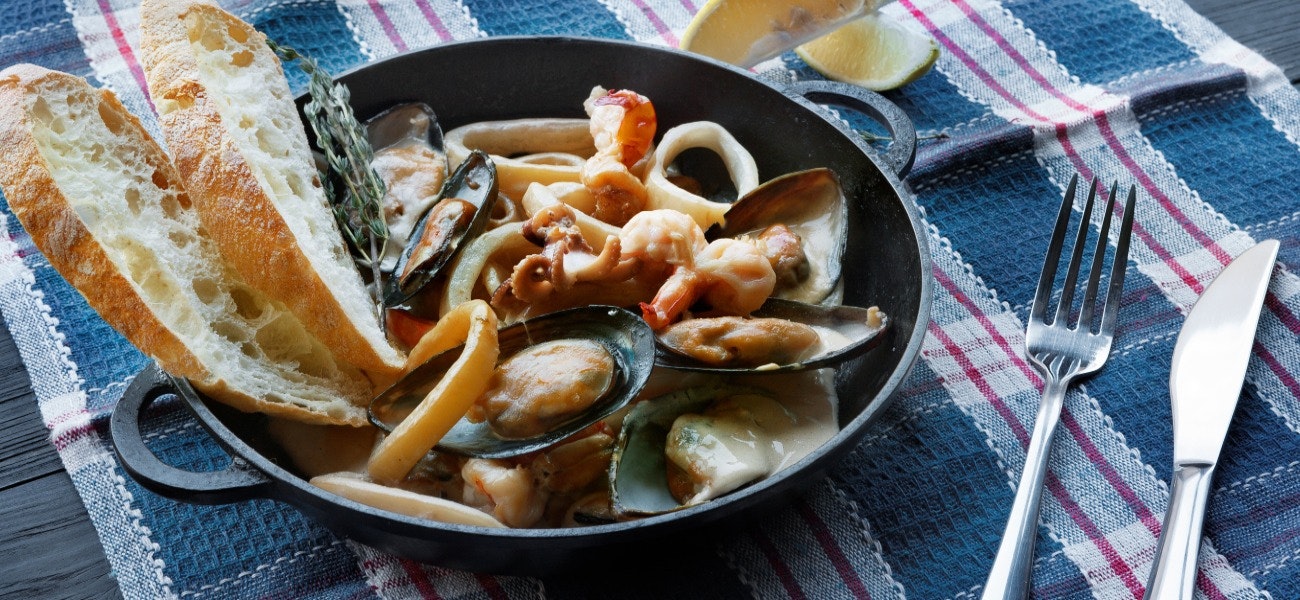 Seafood Stew in Saucepan. Authentic italian restaurant cuisine, healthy delicatessen food. Oysters, shrimps, calamari in white cream sauce with bruschetta. Bowl closeup on served table