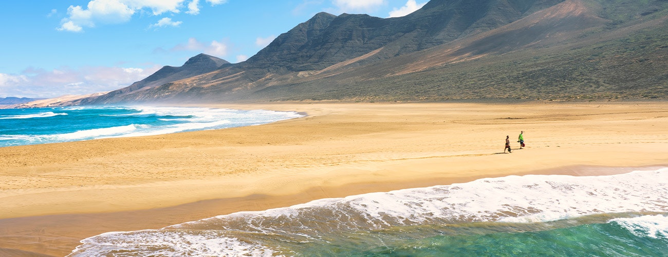 Two people walking on a vast sandy beach in Spanish Canary Island Fuerteventura