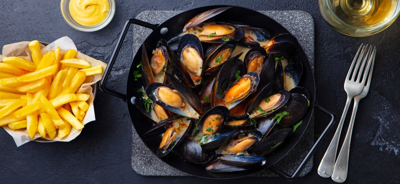 Mussels with french fries and white wine in cooking pan. Grey background. Top view.