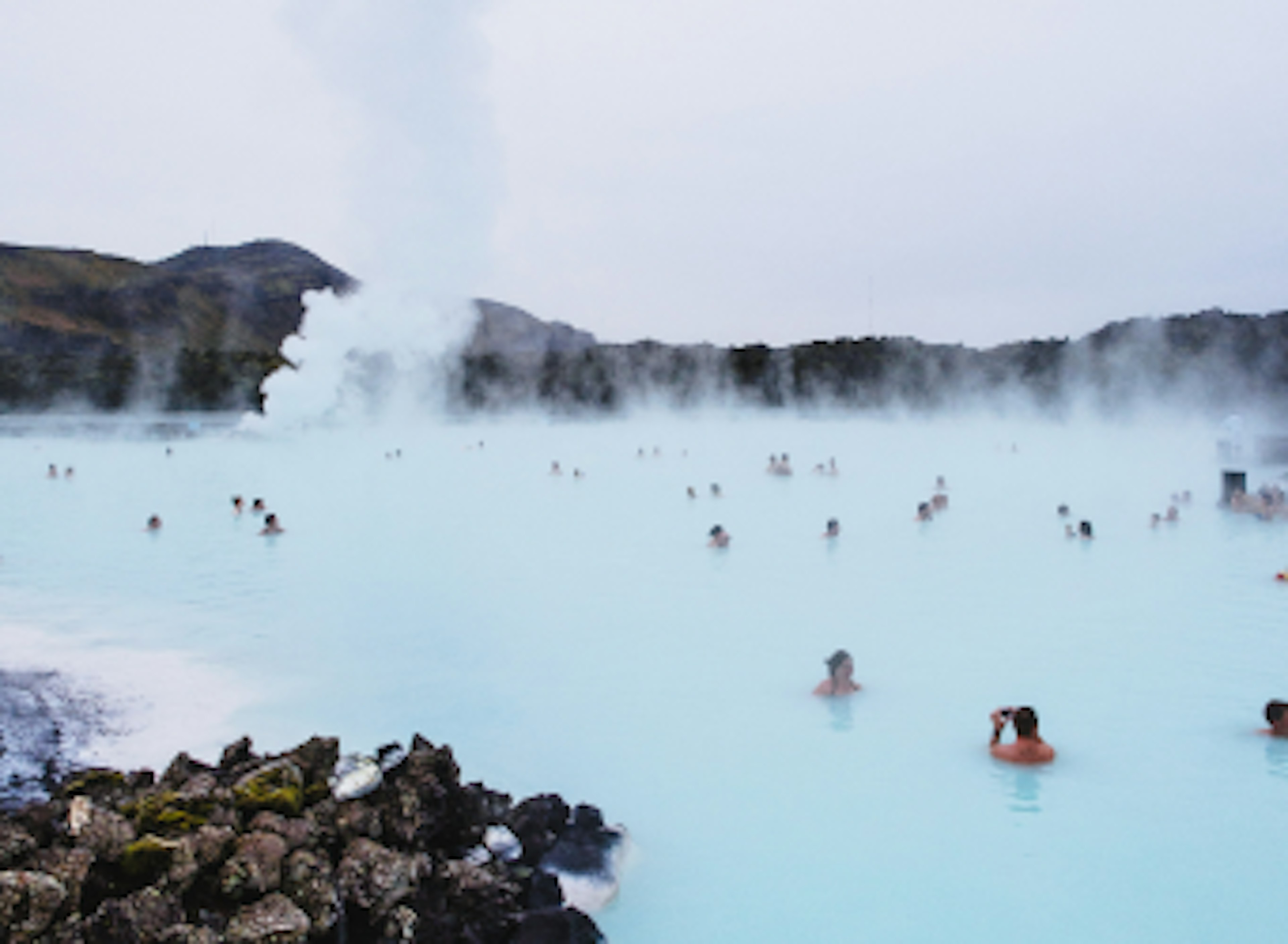 A view over a hot spring in Iceland full of people in the steamy waters