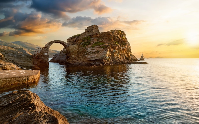 The old arched stone bridge leading to the ancient Castle of Andros island at the Cyclades of Greece during a beautiful summer sunrise