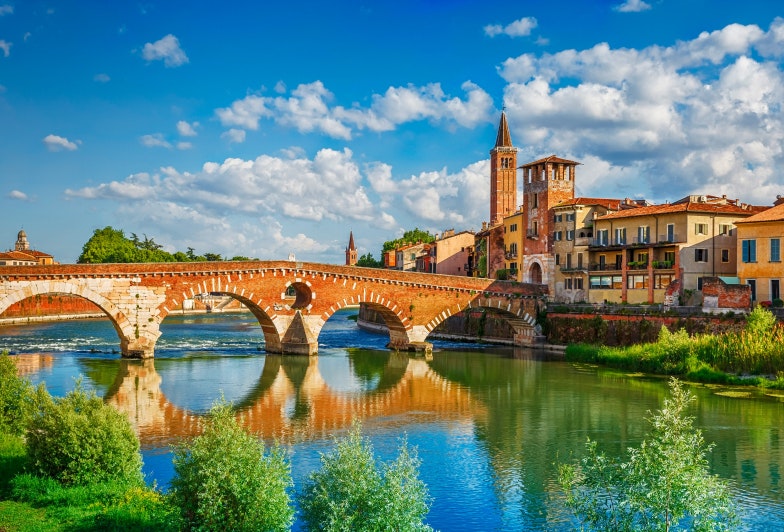 Panoramic view to Bridge Ponte Pietra in Verona on Adige river. Veneto region. Italy. Sunny summer day panorama and blue dramatic sky with clouds. Ancient european italian terracotta color houses