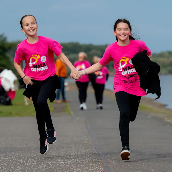 Two kids smiling and running hand-in-hand, wearing Walk of Hope t-shirts.