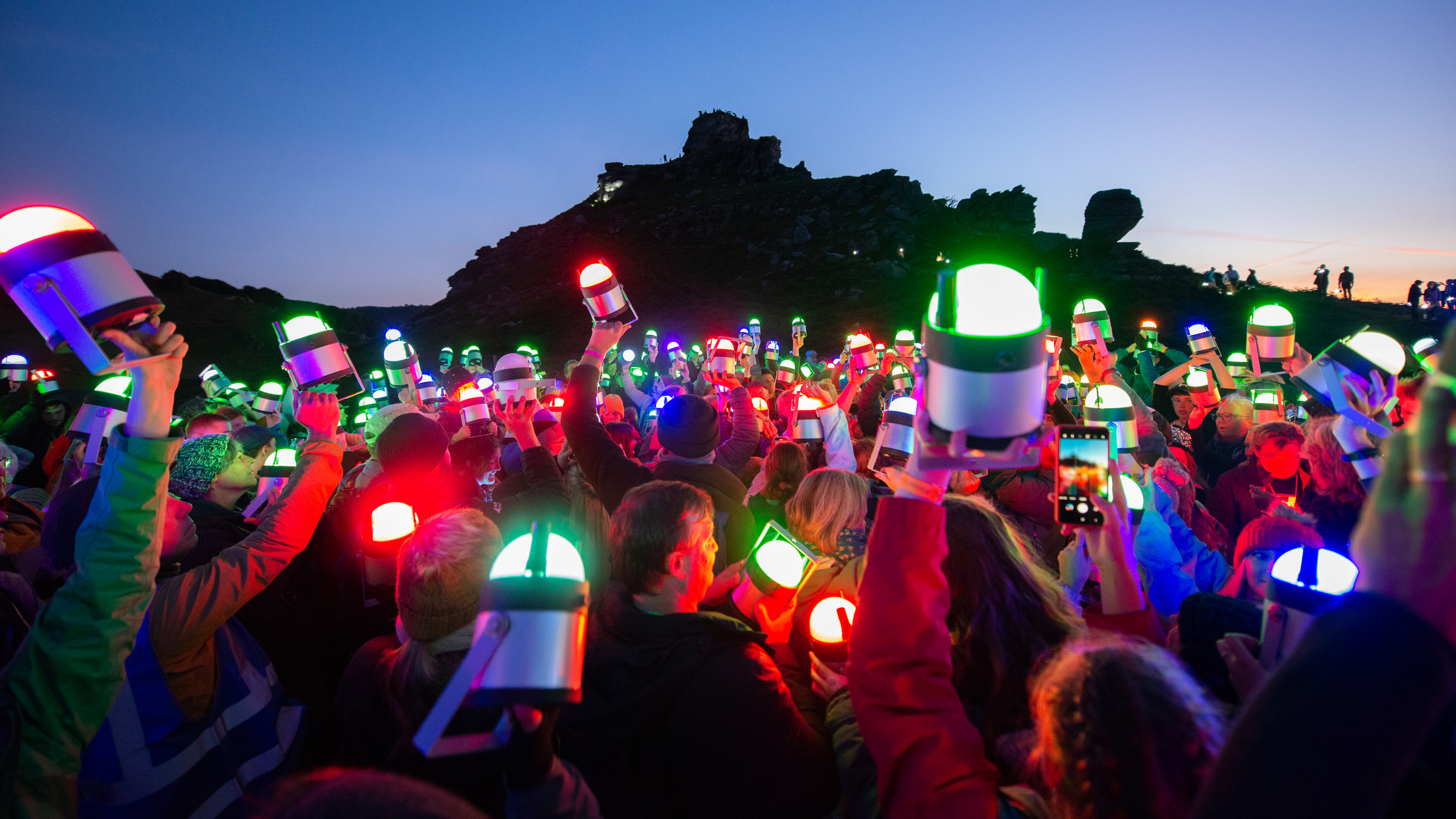 Lumenators holding up their geolights into the sky, lit in different colours as the sun goes down